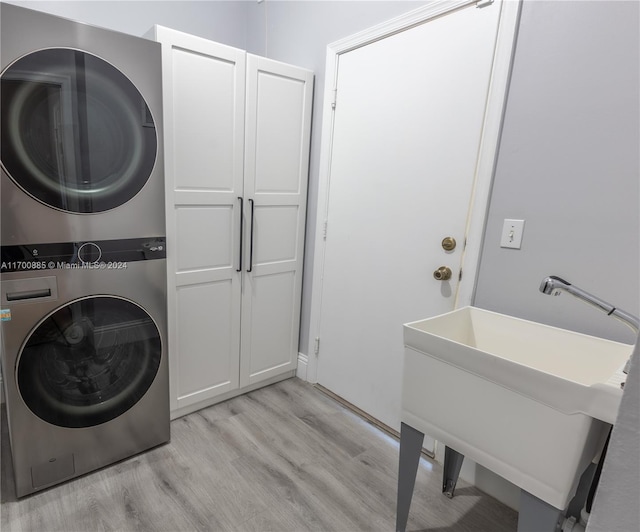 clothes washing area with cabinets, light hardwood / wood-style floors, stacked washer / dryer, and sink