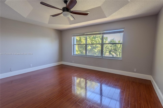 empty room featuring a textured ceiling, ceiling fan, a raised ceiling, and dark wood-type flooring