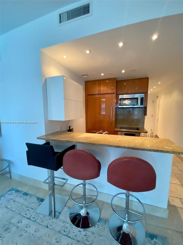 kitchen featuring a breakfast bar, white cabinets, decorative backsplash, paneled built in refrigerator, and kitchen peninsula