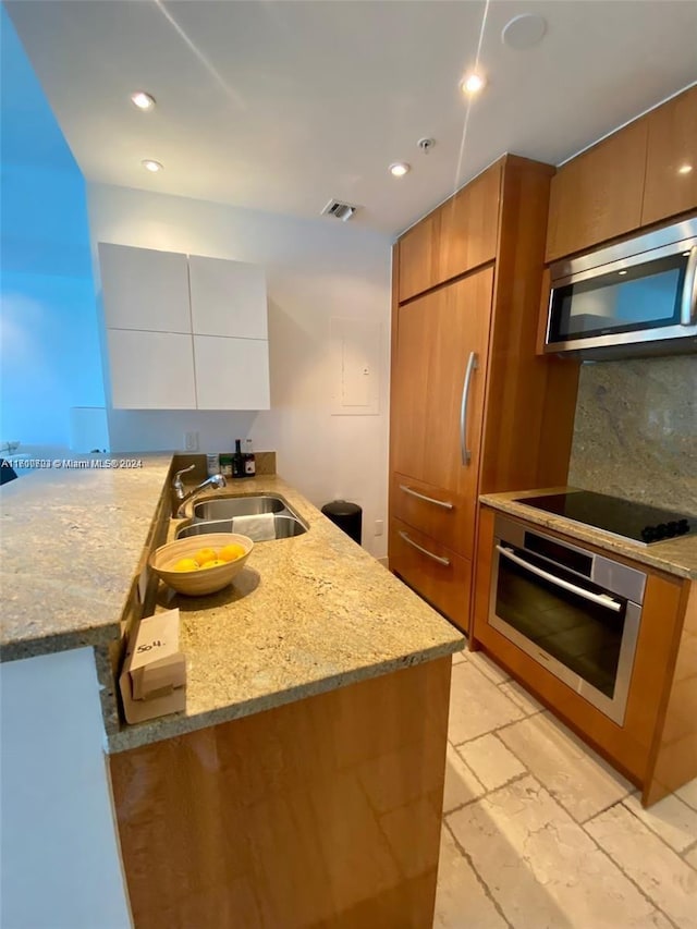 kitchen featuring kitchen peninsula, appliances with stainless steel finishes, light stone counters, and sink