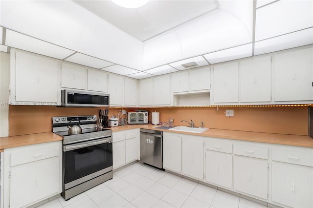 kitchen featuring sink, white cabinets, light tile patterned floors, and appliances with stainless steel finishes