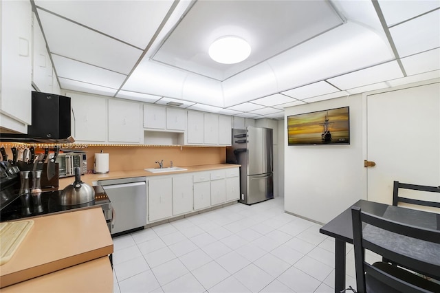 kitchen with appliances with stainless steel finishes, a drop ceiling, sink, light tile patterned floors, and white cabinets