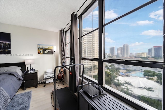 bedroom with a textured ceiling, light wood-style flooring, multiple windows, and a city view