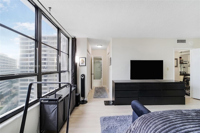 bedroom featuring light wood-style floors, expansive windows, visible vents, and a textured ceiling