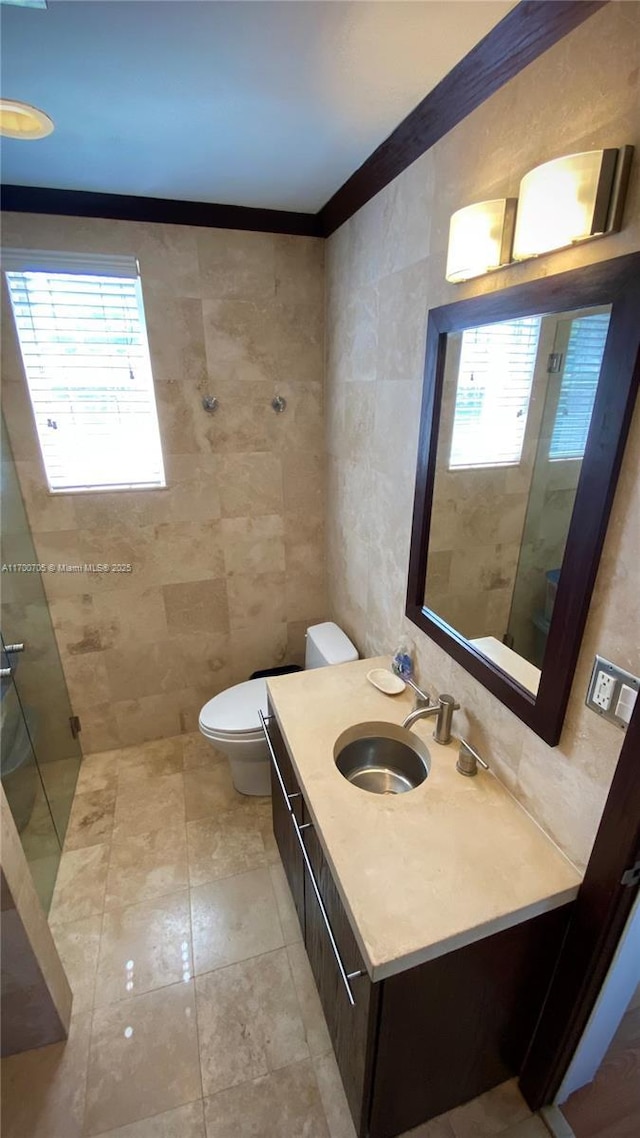 bathroom with tile patterned floors, crown molding, toilet, vanity, and tile walls