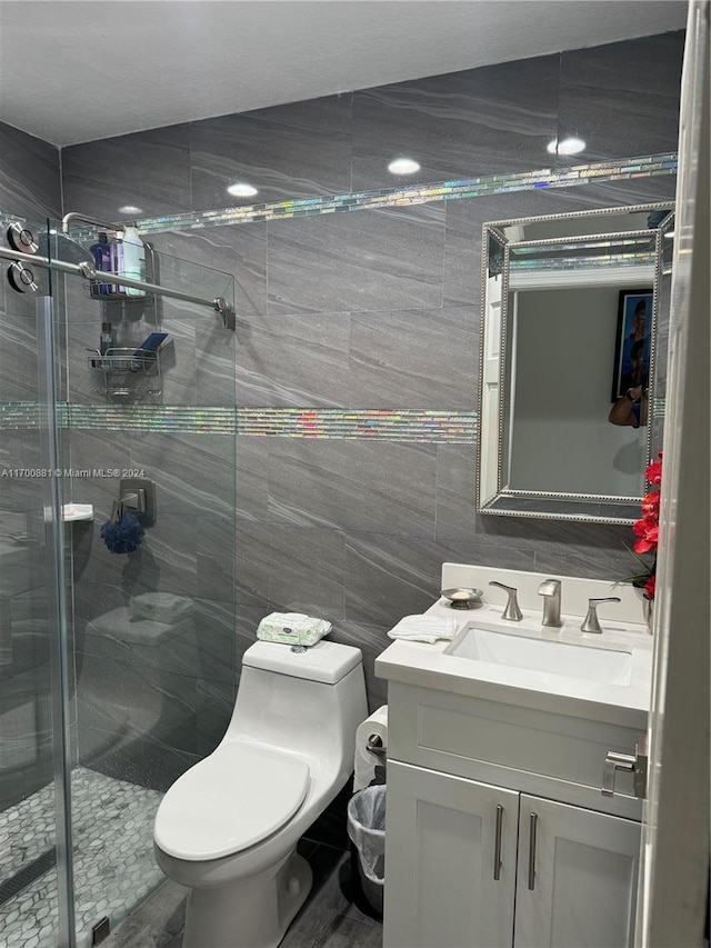 bathroom featuring vanity, a shower with door, toilet, and tile walls