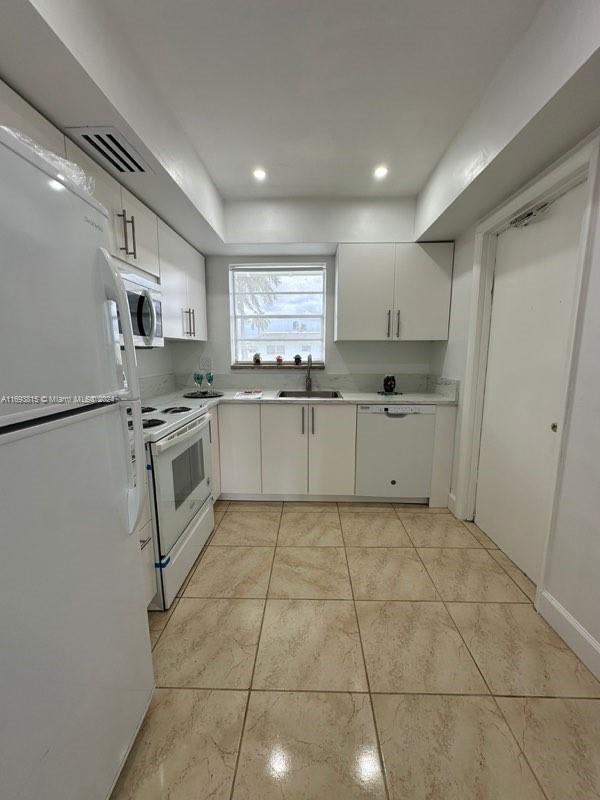 kitchen with white cabinets, white appliances, light tile patterned flooring, and sink