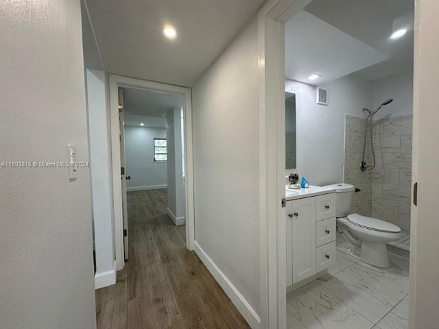 bathroom featuring hardwood / wood-style flooring, toilet, vanity, and tiled shower