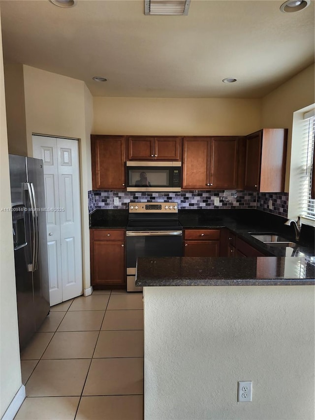 kitchen featuring kitchen peninsula, sink, appliances with stainless steel finishes, light tile patterned floors, and dark stone counters