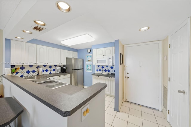 kitchen featuring stainless steel refrigerator, light tile patterned flooring, kitchen peninsula, decorative backsplash, and white cabinets