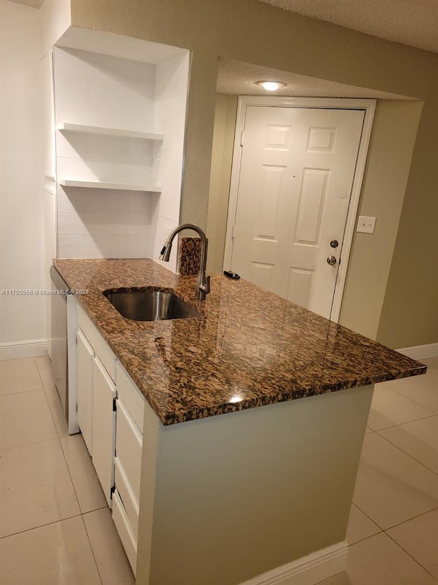 kitchen with light tile patterned flooring, dark stone countertops, white cabinetry, and sink