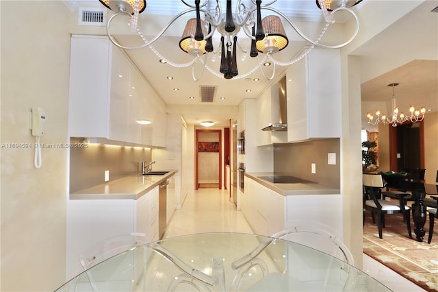 kitchen with sink, an inviting chandelier, appliances with stainless steel finishes, white cabinets, and wall chimney range hood