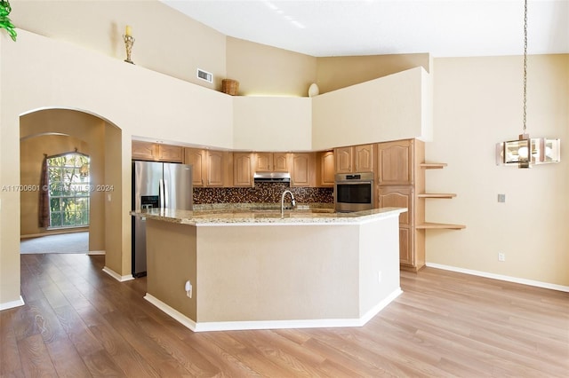 kitchen with a kitchen island with sink, high vaulted ceiling, appliances with stainless steel finishes, decorative light fixtures, and light hardwood / wood-style floors