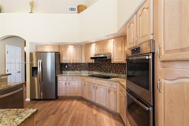 kitchen featuring light stone countertops, light brown cabinets, a towering ceiling, and appliances with stainless steel finishes