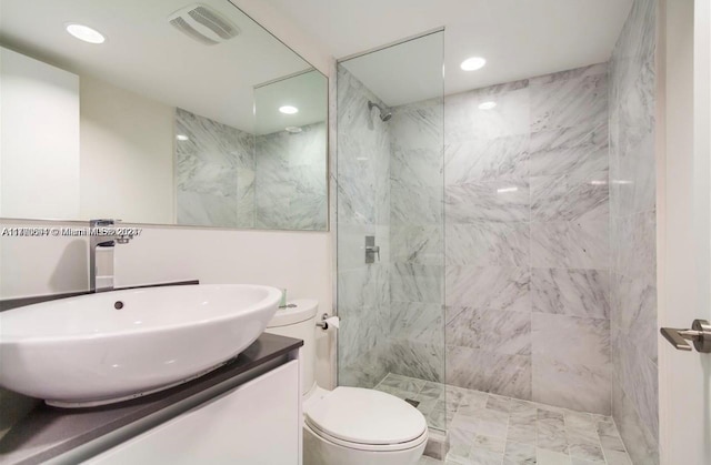 bathroom with toilet, a tile shower, and vanity