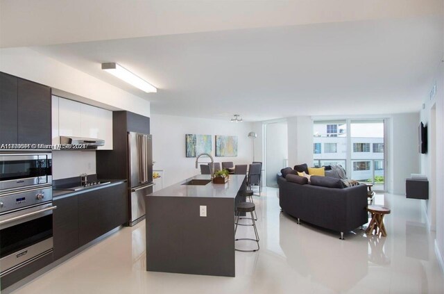 kitchen featuring sink, stainless steel appliances, an island with sink, extractor fan, and a breakfast bar area