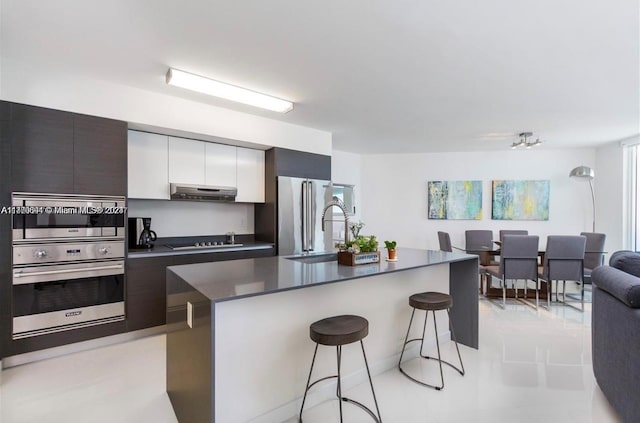 kitchen featuring high end refrigerator, ventilation hood, sink, a kitchen bar, and white cabinetry