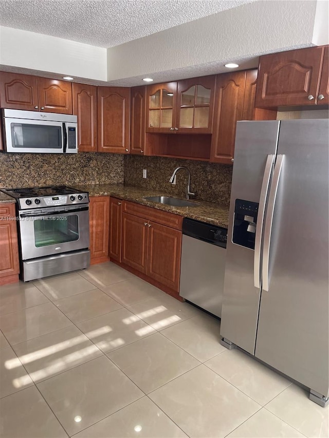 kitchen featuring light tile patterned flooring, appliances with stainless steel finishes, sink, dark stone countertops, and decorative backsplash