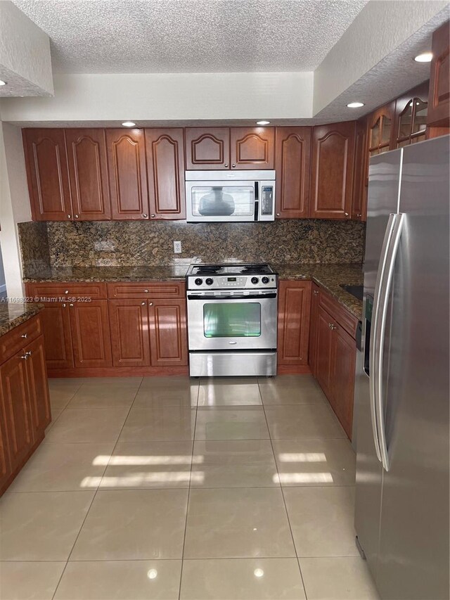 kitchen featuring light tile patterned flooring, dark stone countertops, backsplash, stainless steel appliances, and a textured ceiling