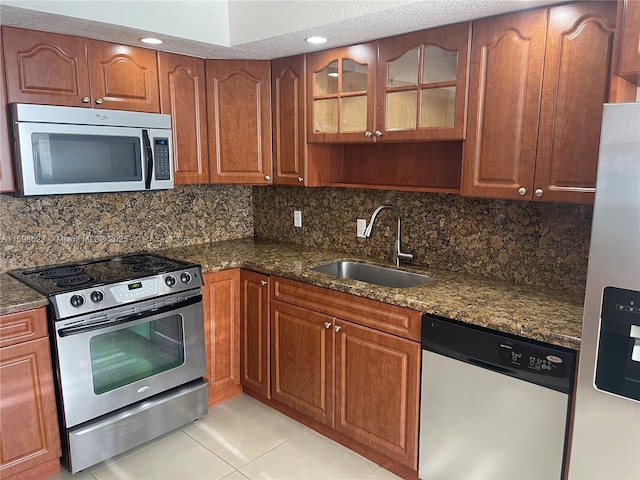 kitchen with sink, appliances with stainless steel finishes, tasteful backsplash, light tile patterned flooring, and dark stone counters