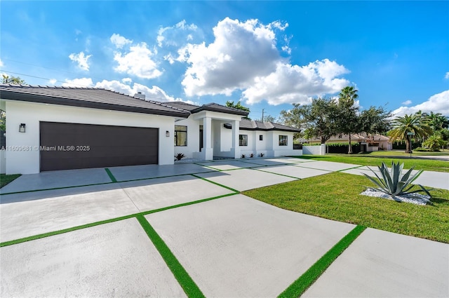 prairie-style home with a garage, concrete driveway, a front yard, and stucco siding