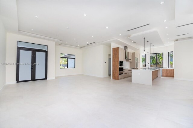 kitchen featuring wall chimney exhaust hood, plenty of natural light, an island with sink, and hanging light fixtures