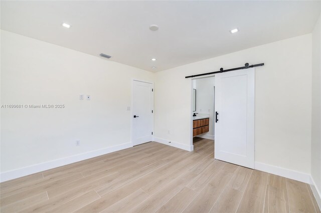 unfurnished bedroom with a walk in closet, light wood-type flooring, a closet, and a barn door