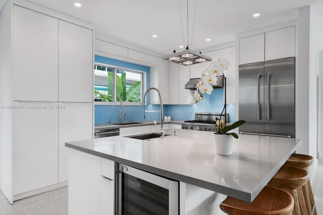 kitchen with pendant lighting, a center island with sink, appliances with stainless steel finishes, white cabinetry, and beverage cooler