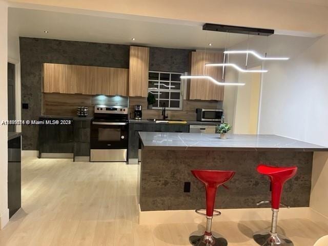 kitchen featuring a kitchen bar, stainless steel appliances, sink, pendant lighting, and light hardwood / wood-style flooring