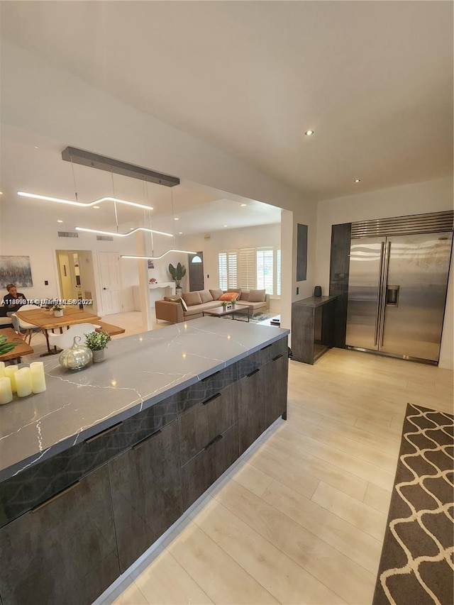 kitchen with light stone countertops, dark brown cabinets, light hardwood / wood-style flooring, and stainless steel built in fridge