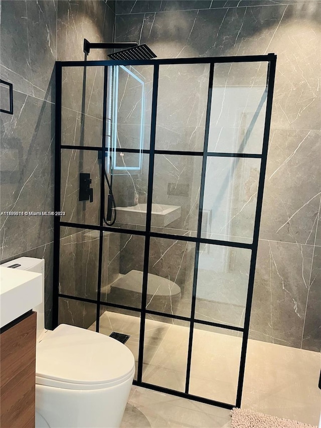 bathroom with a tile shower, vanity, tile walls, and toilet