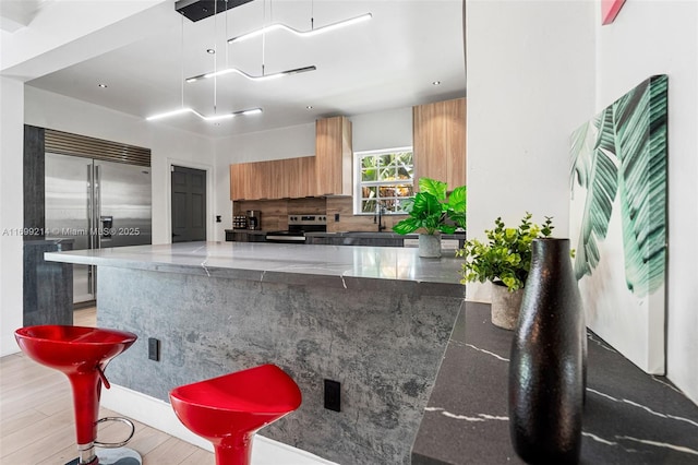 13751 NE 1st Ave, Miami, FL 33161 - kitchen with stainless steel appliances, light wood-type flooring, tasteful backsplash, a peninsula, and brown cabinets