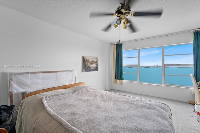 bedroom featuring carpet, ceiling fan, a water view, and a textured ceiling