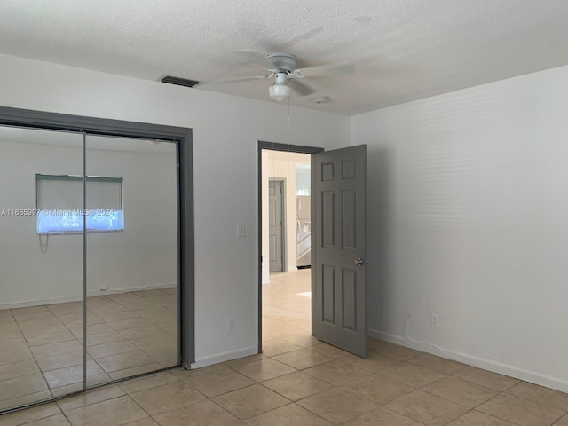 unfurnished bedroom featuring light tile patterned floors, a textured ceiling, a closet, and ceiling fan