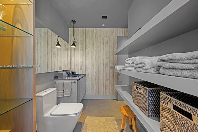 bathroom with wood walls, vanity, concrete floors, and toilet