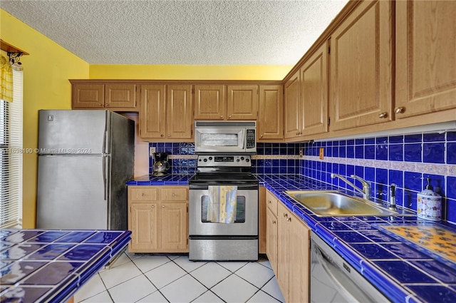 kitchen featuring tasteful backsplash, a textured ceiling, stainless steel appliances, sink, and tile counters