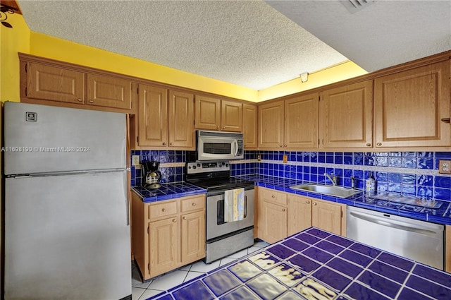 kitchen with sink, backsplash, tile countertops, a textured ceiling, and appliances with stainless steel finishes