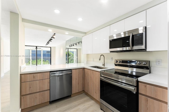 kitchen with appliances with stainless steel finishes, rail lighting, sink, white cabinets, and light hardwood / wood-style floors