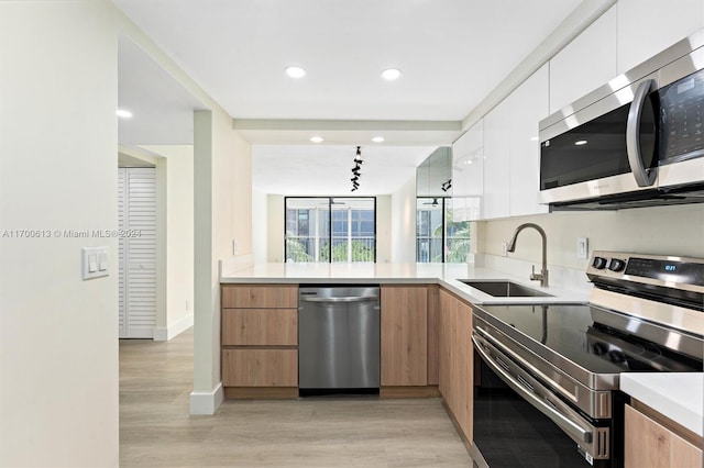 kitchen featuring sink, stainless steel appliances, light hardwood / wood-style floors, track lighting, and white cabinets