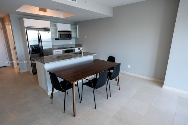 kitchen featuring appliances with stainless steel finishes, a kitchen breakfast bar, sink, dark stone countertops, and white cabinets