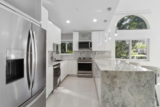 kitchen with pendant lighting, tasteful backsplash, white cabinets, stainless steel appliances, and light stone countertops