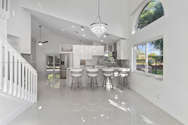 kitchen featuring decorative light fixtures, white cabinets, a kitchen bar, a high ceiling, and stainless steel appliances