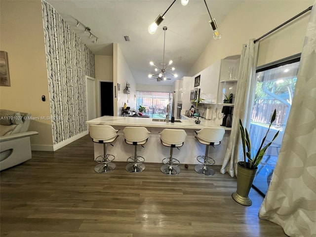 kitchen with kitchen peninsula, hanging light fixtures, dark hardwood / wood-style floors, white cabinetry, and a breakfast bar area