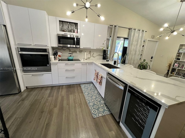 kitchen featuring sink, vaulted ceiling, appliances with stainless steel finishes, a notable chandelier, and white cabinetry