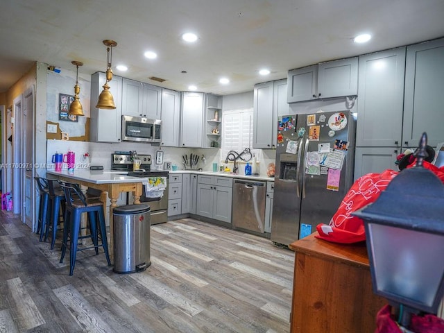 kitchen with a kitchen bar, stainless steel appliances, light hardwood / wood-style flooring, and hanging light fixtures