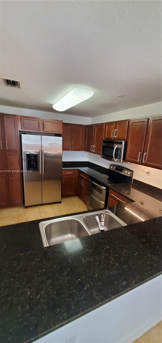 kitchen with sink, dark stone countertops, light tile patterned floors, kitchen peninsula, and stainless steel appliances