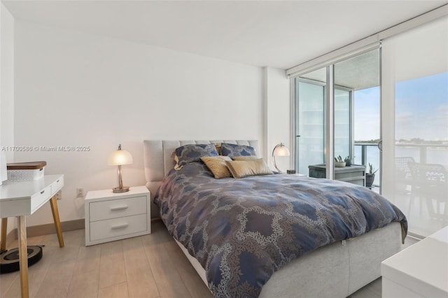 bedroom with a water view, baseboards, light wood-style floors, access to outside, and floor to ceiling windows