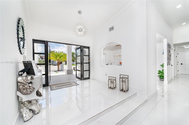 foyer with a notable chandelier, ornamental molding, and french doors