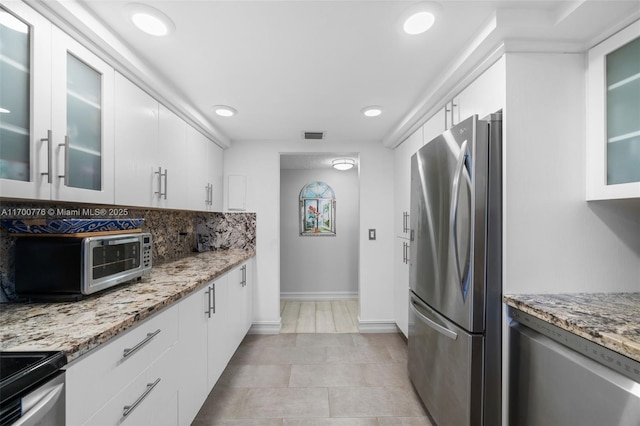 kitchen featuring white cabinets, backsplash, light stone countertops, and stainless steel refrigerator