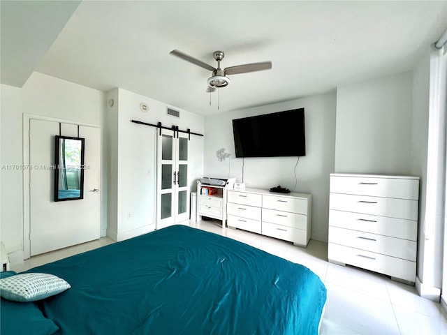 bedroom featuring ceiling fan, a barn door, light tile patterned floors, and a closet